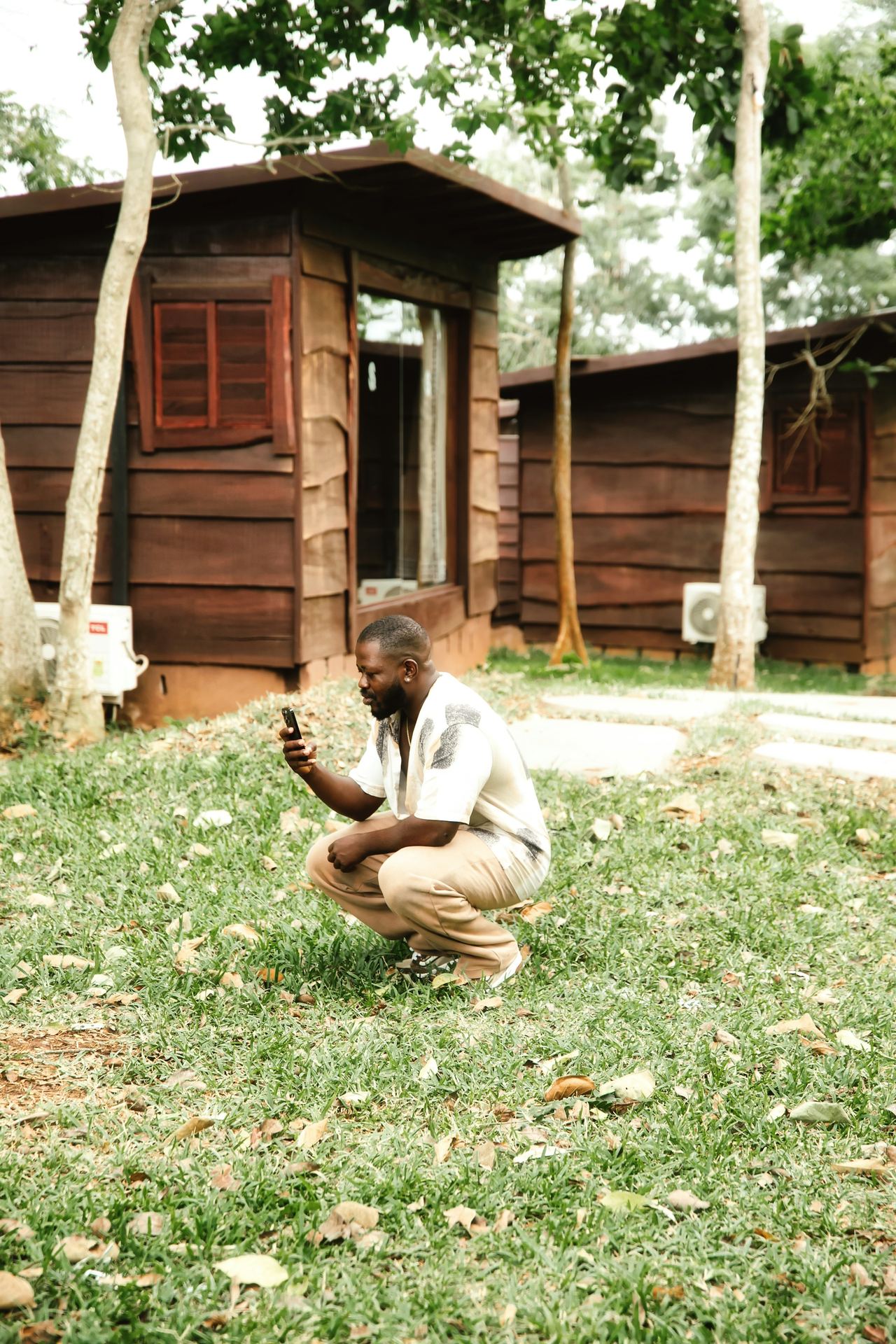 A farmer crouching in grass, checking a phone